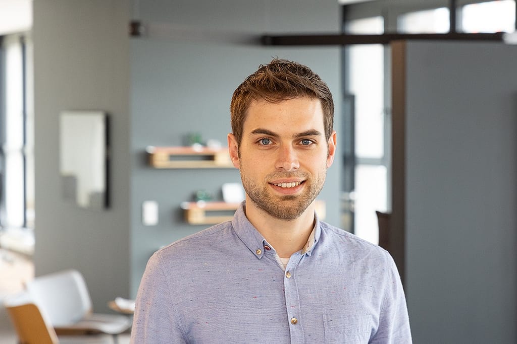 Business Fotografie - Mitarbeiter im Vordergrund. Im Hintergrund ist eine moderne Bürosituation zu sehen