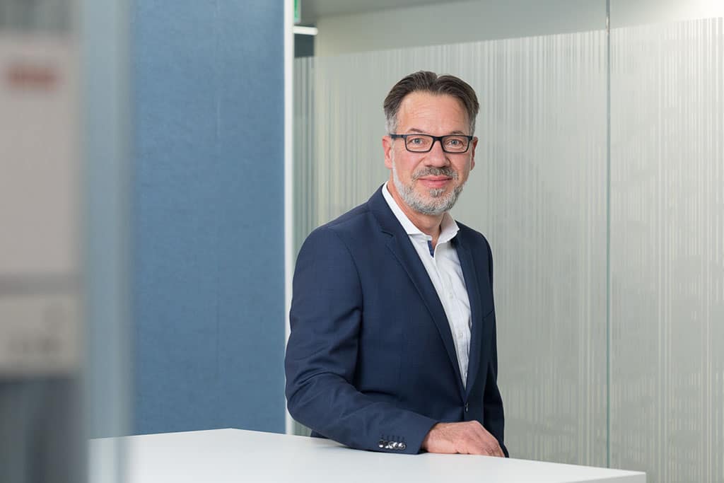 Porträt eines Mannes vor einem grauen Hintergrund.