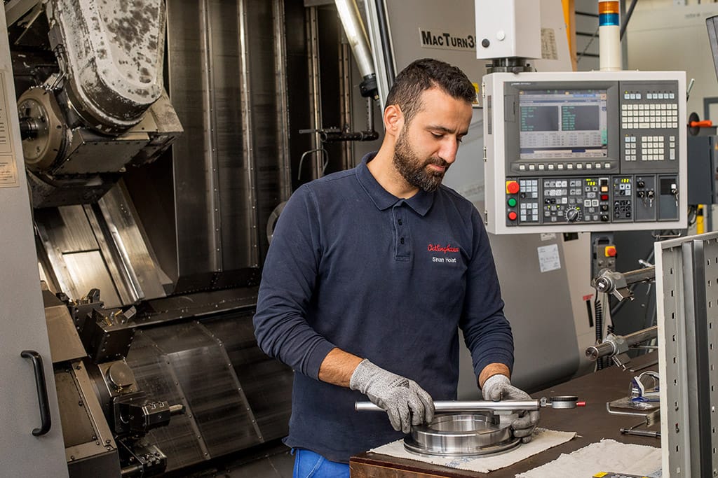 Industriearbeiter in einer Halle. Er bearbeitet ein Metallstück.