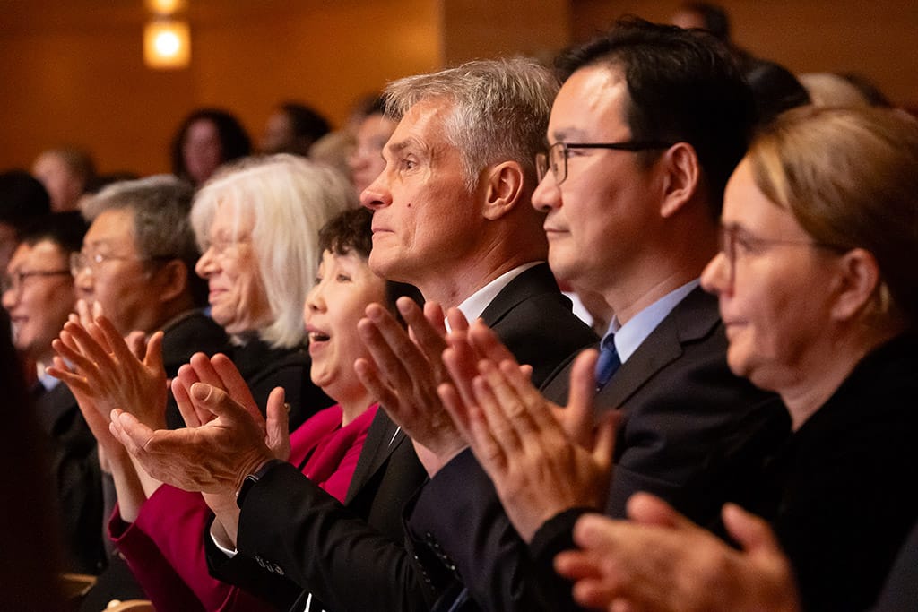 Künstlerfotografie - Der chinesische Chor singt in der Philharmonie Essen, während die Musiker auf der Bühne im Hintergrund ihre Instrumente spielen. Das Publikum ist von der Musik tief bewegt.