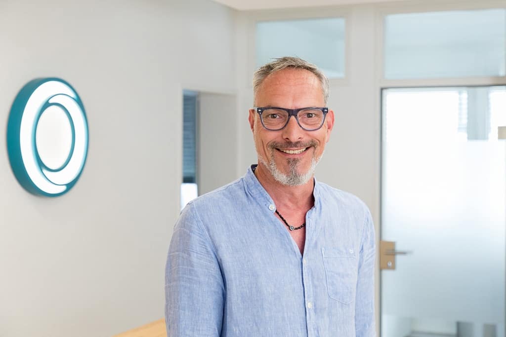 Der Arzt im Porträt, umgeben von einer angenehmen Praxisumgebung – ein Bild, das die persönliche und fürsorgliche Seite der Hausarztmedizin zeigt