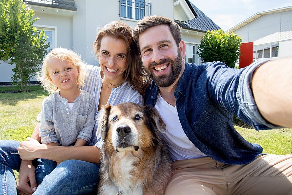 Werbefoto einer Familie die vor einem Haus sitzt, mit Hund und Kind. Es ist Sommer!