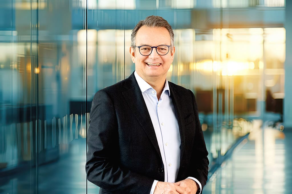 Der CEO von Cosmoings präsentiert sich vor einem futuristischen KI-Hintergrund, der die innovative Ausrichtung des Unternehmens widerspiegelt