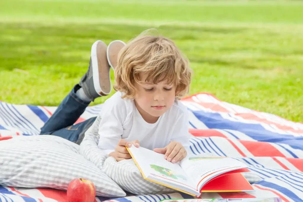 Ein Kind liegt auf dem Rasen und ließt ein Buch