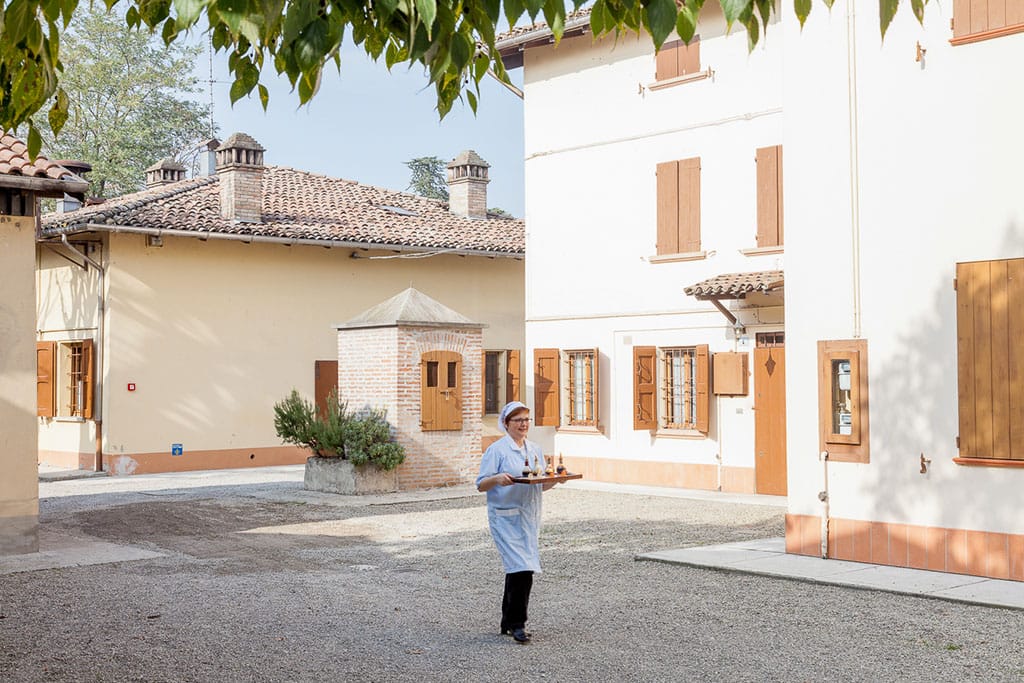 Reisefotograf - Frau bringt Speisen in ein Haus. Der Hof ist sonnendurchflutet.