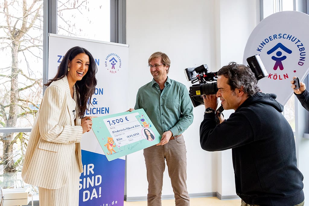 Der KInderschutzbund in Köln bekommt von Rebecca Mir einen Scheck überreicht.