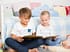 Zwei Kinder sitzen in einem Kinderzimmer und lesen ein Buch.