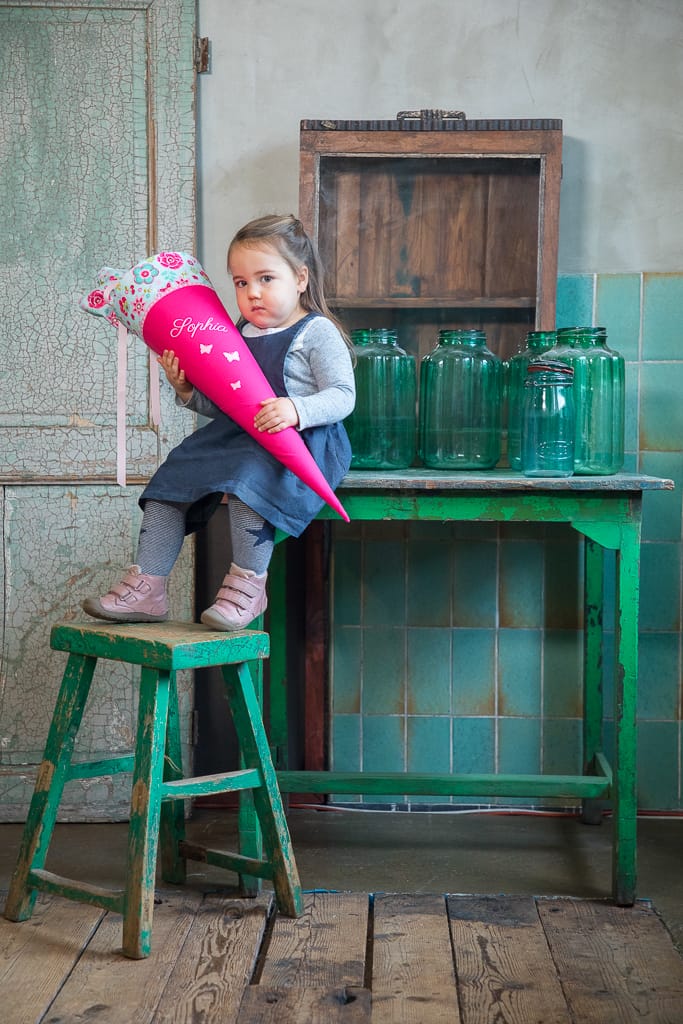 Ein Kind sitzt auf dem Tisch und hält eine Schultüte in der Hand